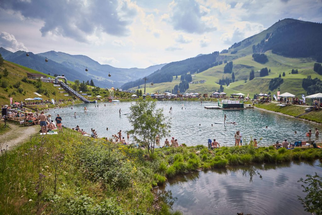 Sommer-Event am See in Saalbach Hinterglemm mit vielen Badenden und umgebenden Ständen.
